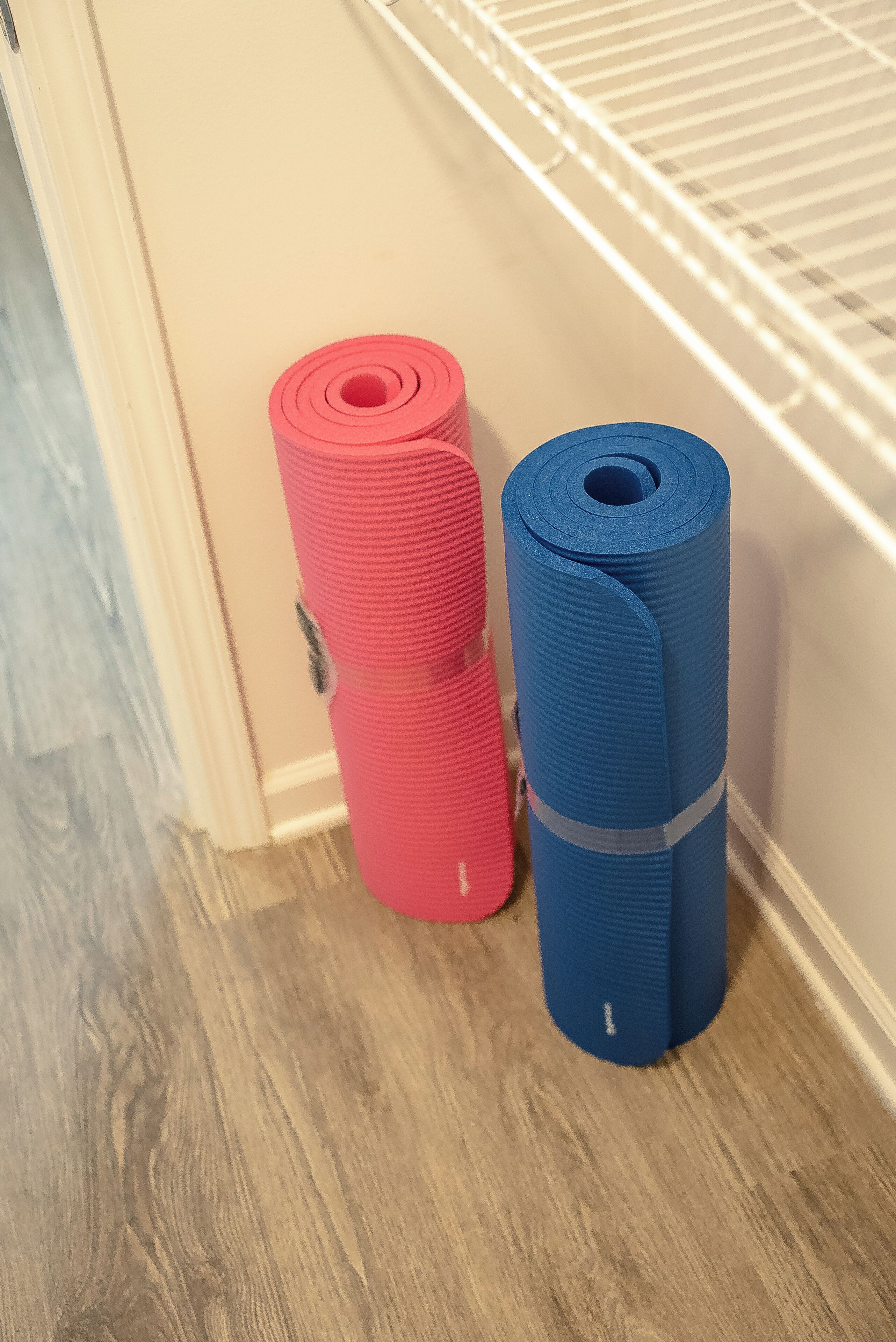 Deux tapis de yoga, un rouge et un bleu, sont empilés contre un mur dans une pièce dont le sol est recouvert de planches de bois.