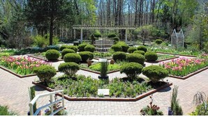 Un jardín formal con topiarios simétricos, una fuente central y un pérgola.
