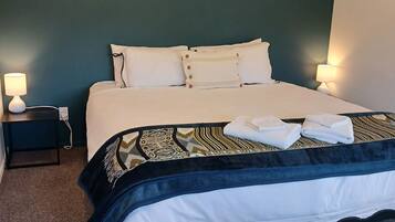 Una cama bien hecha con sábanas blancas, un plaid estampado y dos lámparas de noche.