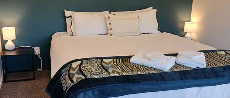 Una cama bien hecha con sábanas blancas, un plaid estampado y dos lámparas de noche.