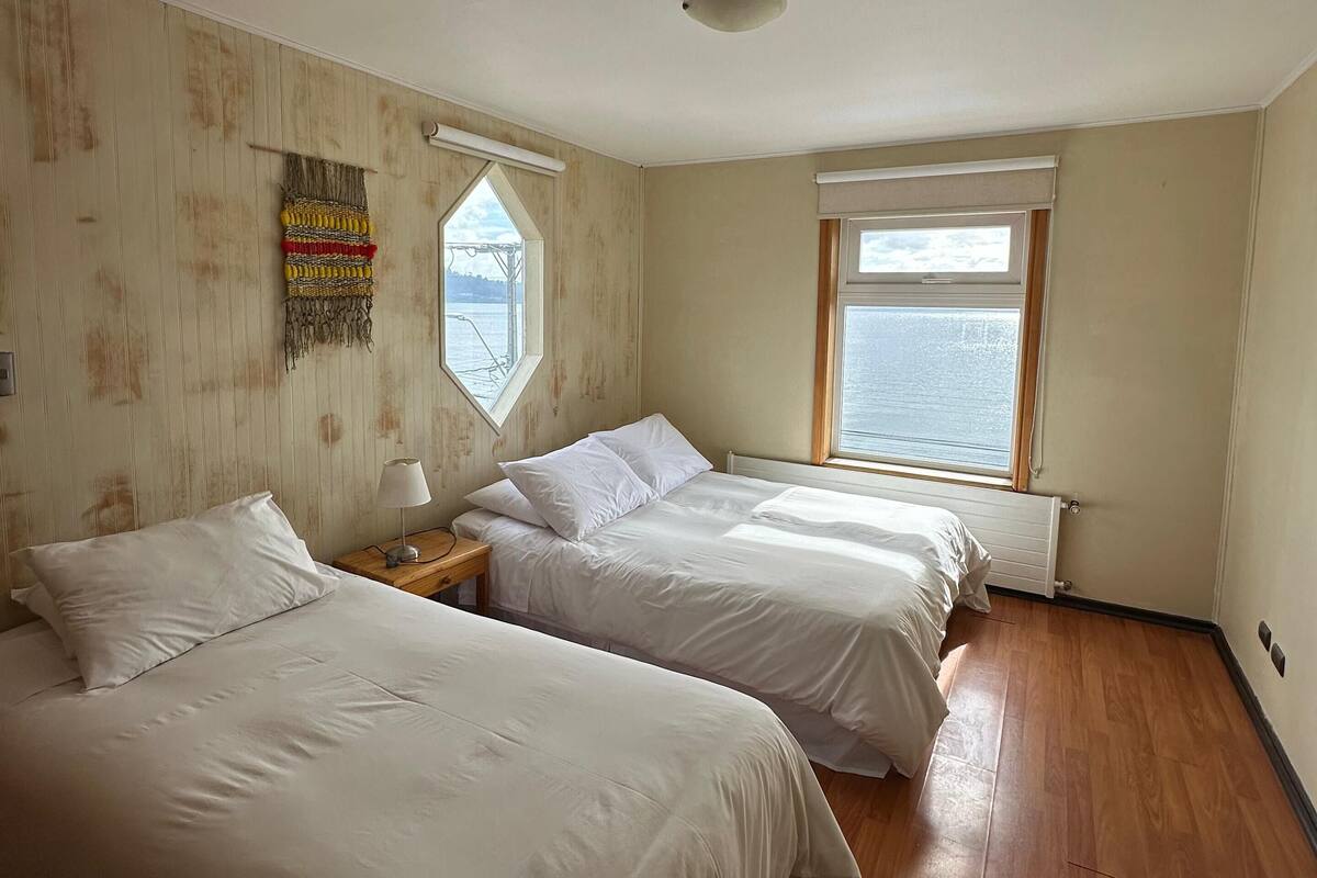 Ein Zimmer mit zwei Betten, Holzboden, einem Fenster mit Aussicht und einer Deckenleuchte.