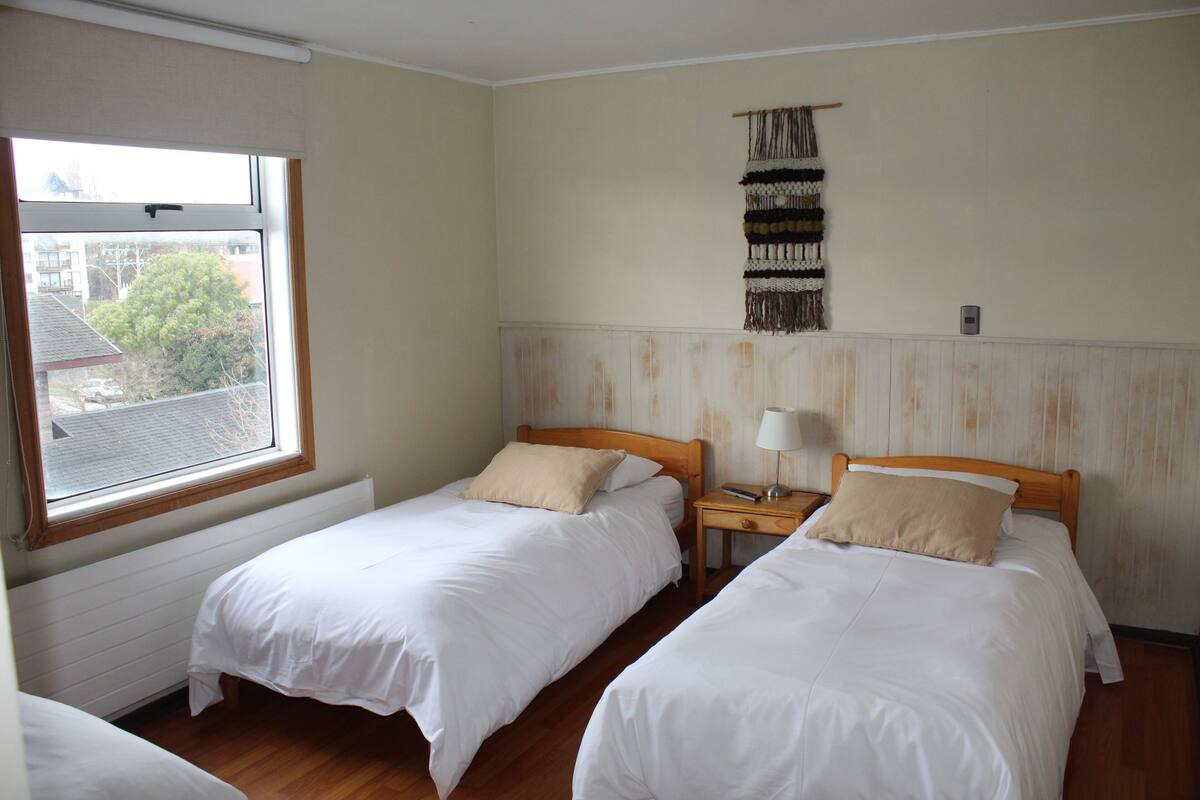 Ein Zimmer mit zwei Einzelbetten, einem Fenster, einer Wandteppich und einem Nachttisch mit Lampe.
