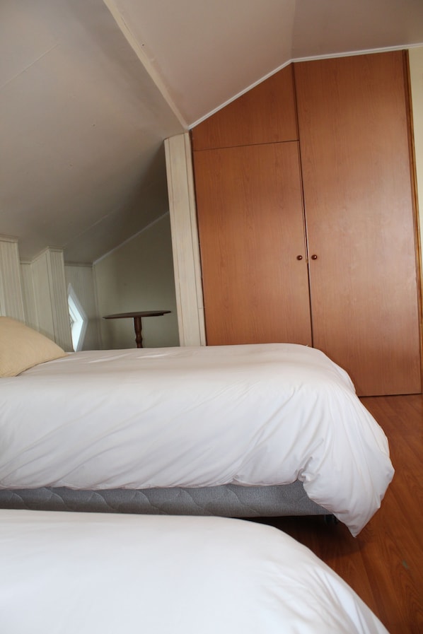 A bedroom with two beds, wooden wardrobe, and a small table. - Hotel Casona Freire (Puerto Varas)