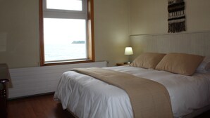 Un dormitorio con una cama grande, una ventana con vistas, una lámpara de noche y un tapiz colgado en la pared.