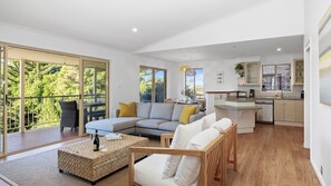 A modern living room with a grey sectional sofa, a wooden coffee table, and a balcony with a wicker chair. - Seahaven in Mollymook (Mollymook Beach)