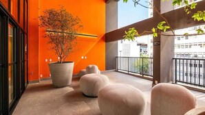 Ein Balkon mit einem Topfbaum, einer großen Pflanze im Topf und mehreren Sitzbereichen mit runden Sitzgelegenheiten.