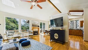 Un salón amplio con chimenea, televisor y un ventanal grande con vistas a un bosque.