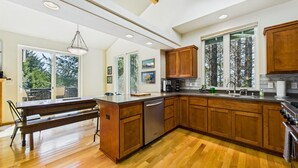 Una cocina amplia con armarios de madera, una isla central y grandes ventanales con vistas a árboles.
