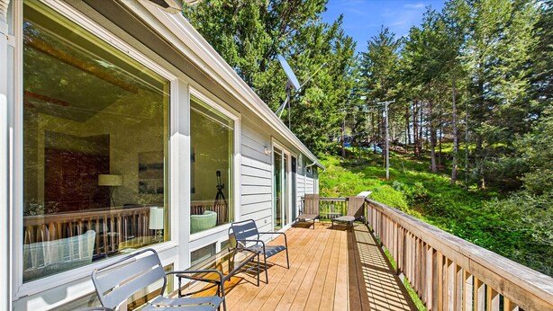 Una terraza de madera con mobiliario exterior, ventanas amplias y vistas a una ladera boscosa.