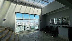 Un balcón amplio con vista a la ciudad, un espacio de descanso con sillas y un ventanal grande.