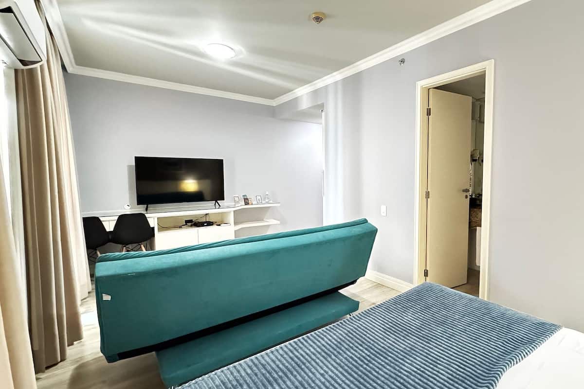 Una habitación de hotel moderna con un sofá color turquesa, un televisor de pantalla plana y un ventanal amplio.