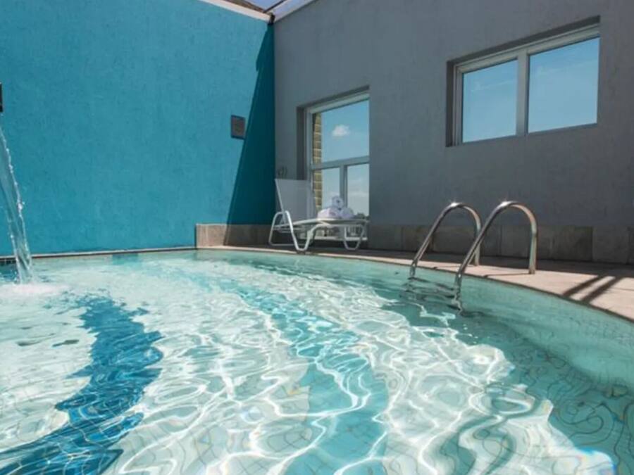 Una piscina con agua cristalina, una fuente y una tumbona.