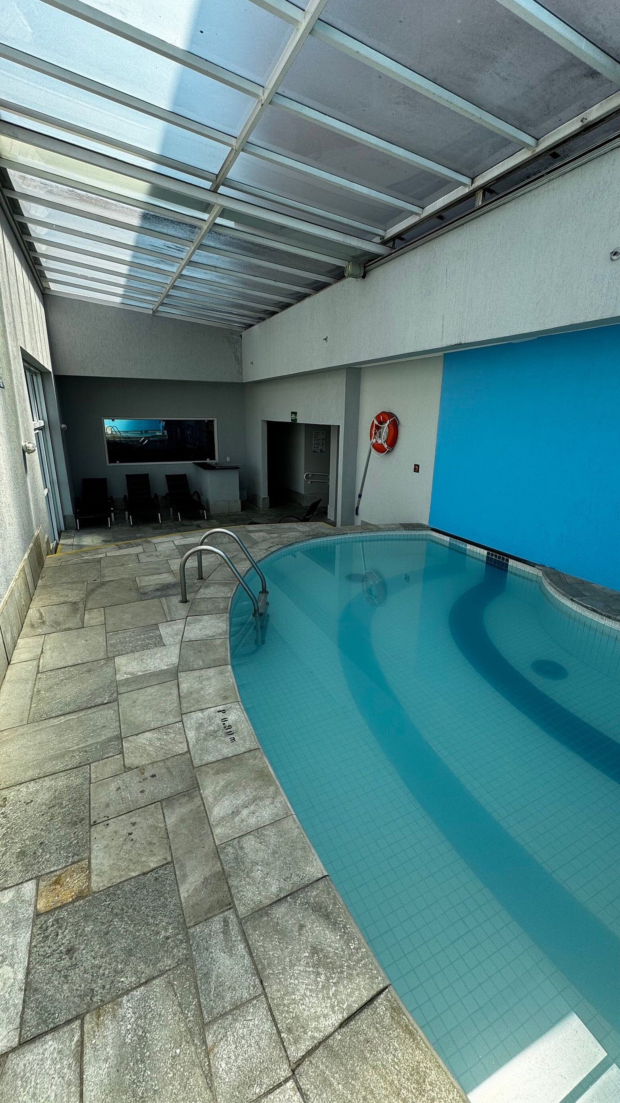 Una piscina interior con techo de vidrio, suelo de piedra y pared azul.