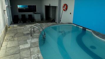 Una piscina interior con techo de vidrio, suelo de piedra y pared azul.