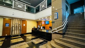 Un vestíbulo de hotel con una recepción, una escalera y un entrepiso.