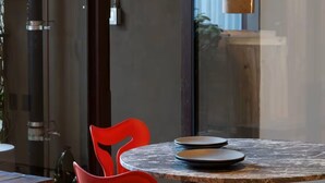 Een moderne eethoek met een ronde tafel, twee rode stoelen en een houten bank.