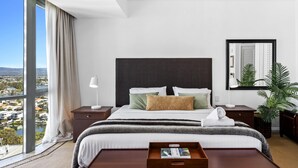 Une chambre d’hôtel moderne avec un grand lit, une table de chevet, une commode, un miroir et une vue sur la ville.