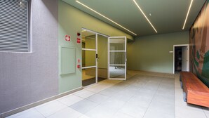 Un pasillo con pared verde, un detector de incendios, un banco de madera y una puerta que da a una habitación.