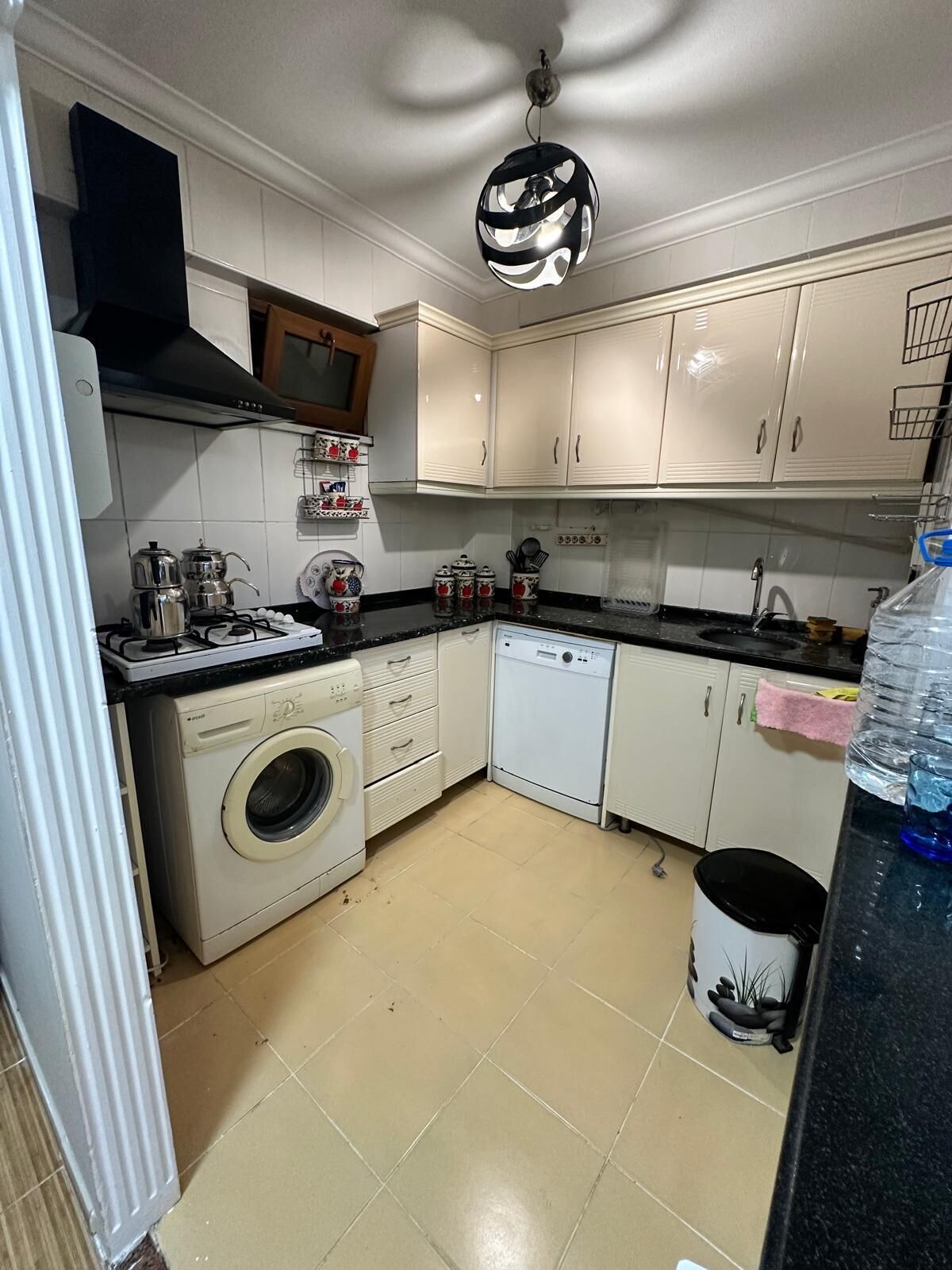 Een praktische keuken met witte kastjes, een wasmachine, een vaatwasser en een zwart aanrecht.