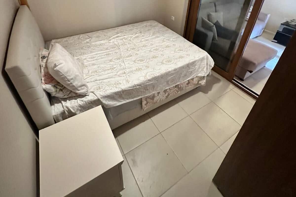 A small, single-bed room with a wooden ceiling and a sliding glass door leading to a balcony.