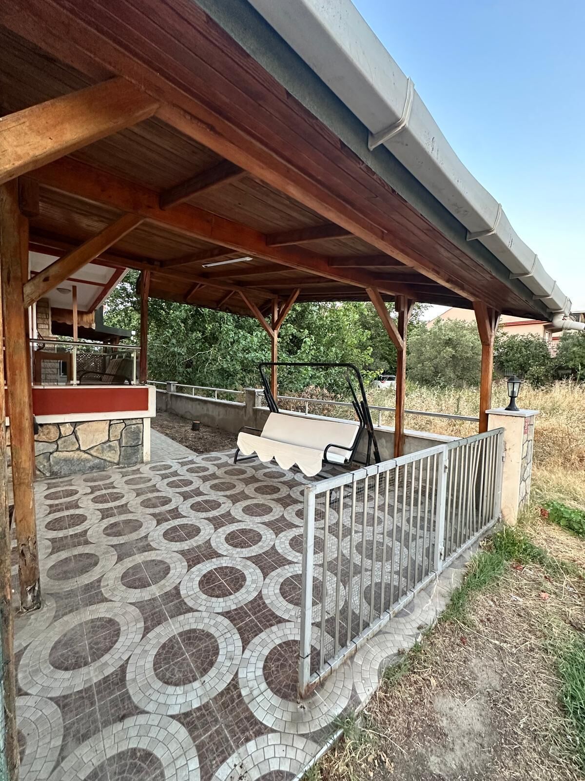 Uma área de pátio coberta com chão de azulejos estampados, um banco e um corrimão.