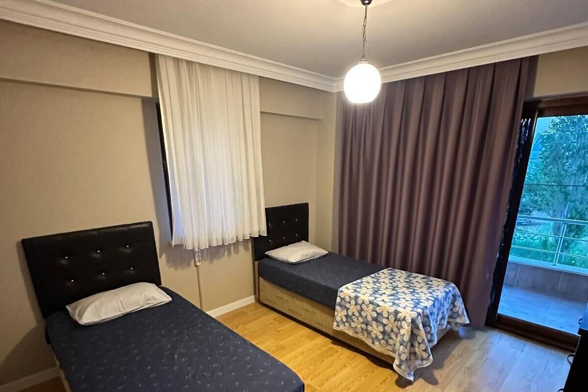 A room with two beds, a ceiling fan, and a large window with curtains.