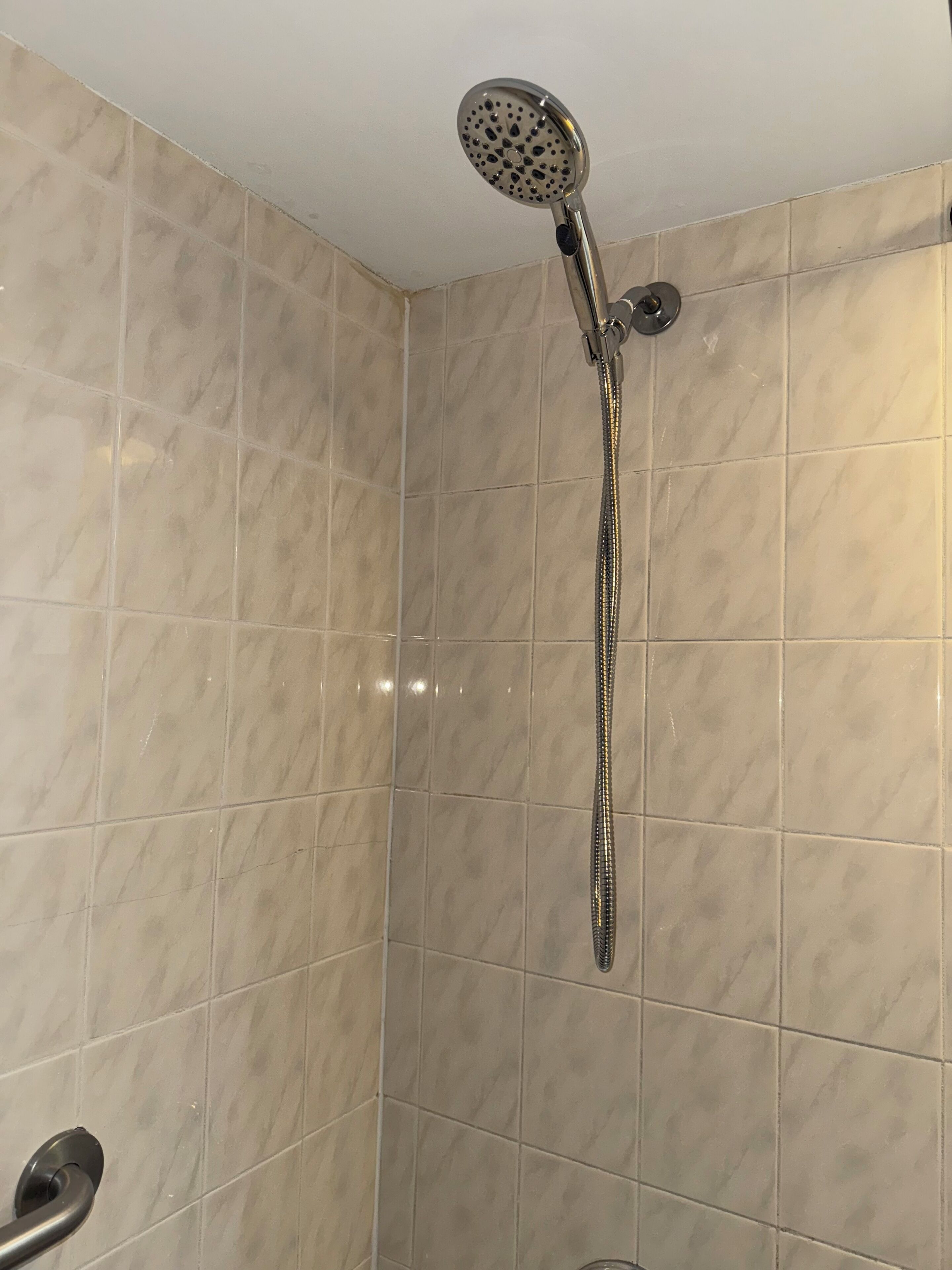 Eine Dusche mit Duschbrause und langem Schlauch in einem Raum mit beige gefliesten Wänden.