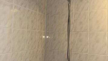 Eine Dusche mit Duschbrause und langem Schlauch in einem Raum mit beige gefliesten Wänden.