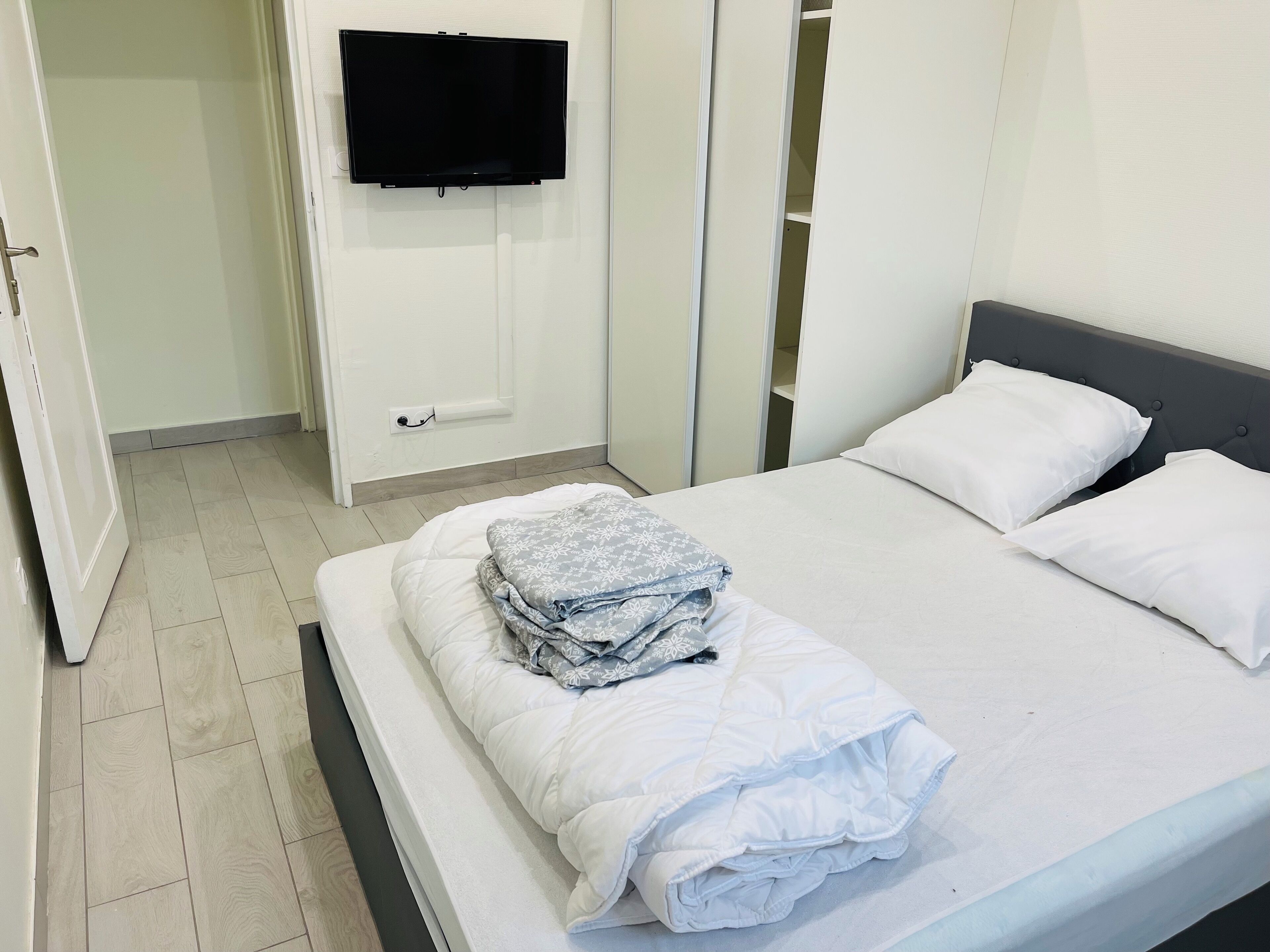 Quarto de hotel com uma cama, televisão presa à parede e um guarda-roupa.
