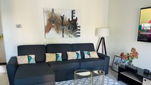 Uma sala de estar moderna com um sofá escuro, almofadas estampadas, um tapete geométrico e um quadro pendurado na parede.