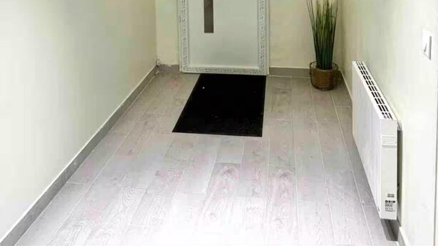 Um corredor com uma porta branca, um tapete preto na entrada e um radiador à direita.