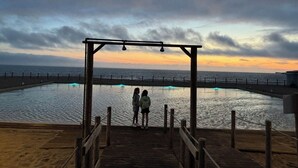 A wooden pier leading to a pool with a sunset view.