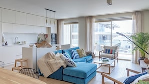 A modern living room with a blue sofa, a wooden coffee table, and a dining area with a wooden table and chairs.