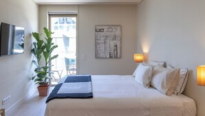 A hotel room with a bed, a potted plant, a painting, and a TV on the wall.