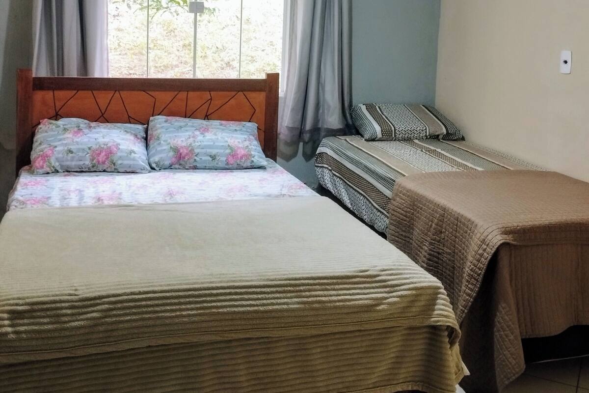 A bedroom with a bed, a bedside table, a nightstand, a window with curtains, and a ceiling fan.