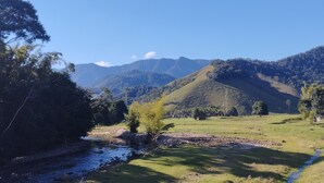 A rural landscape with a river, grassy fields, and hills in the background. - Pousada Solar Bananeiras (Silva Jardim)