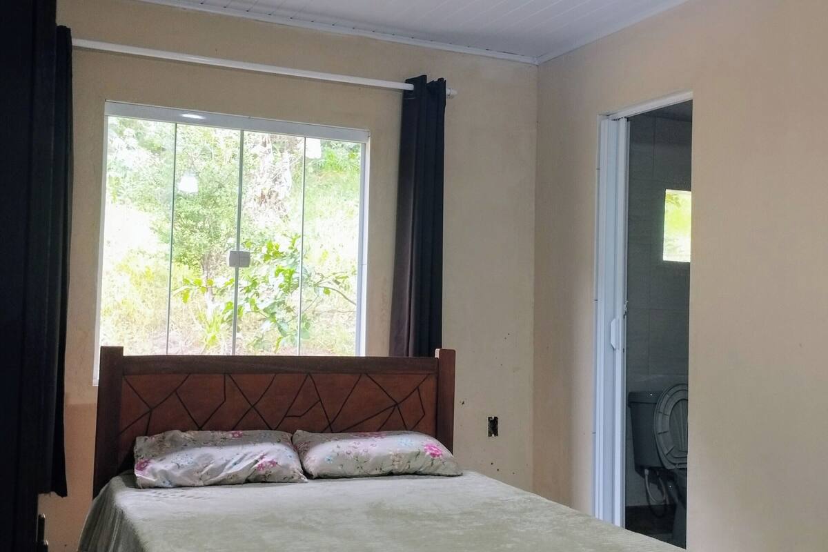 A bedroom with a bed, a ceiling fan, a window with curtains, and a door leading to a bathroom.