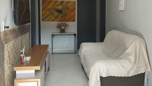 A hotel room with a bed, a desk with a chair, a TV mounted on the wall, and a painting on the wall. - Pousada Solar Bananeiras (Silva Jardim)