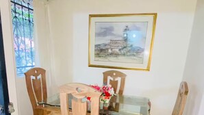 A dining area with a glass-top table, wooden chairs, and a framed picture on the wall.