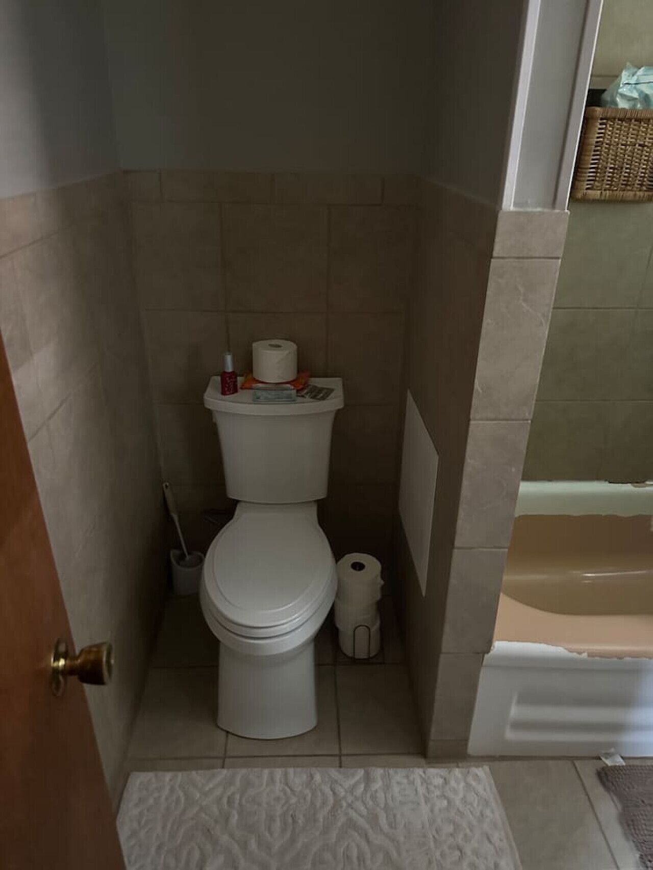 A small bathroom with a toilet, a roll of toilet paper, a cleaning brush, and a small trash bin.