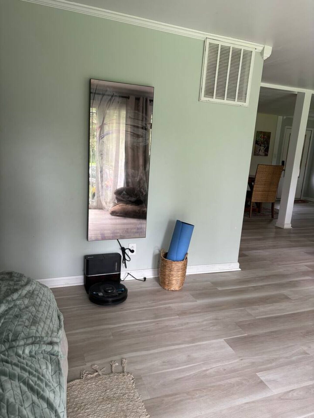 Een kamer met een bed, een groot schilderij, een speaker en een yogamat in een mand.