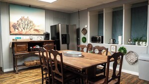A dining area with a wooden table and chairs, a refrigerator, microwave, and a kitchen counter with various items. - Beautiful sleeps 6 apartment, walking distance to Downtown Pilot Mountain Unit 1 (Pilot Mountain)