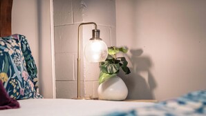 A bedside table with a lamp, a potted plant, and a floral pillow. - Beautiful sleeps 6 apartment, walking distance to Downtown Pilot Mountain Unit 1 (Pilot Mountain)