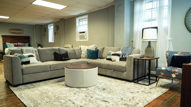 A living room with a sectional sofa, a round ottoman, a small side table, and a floral armchair. - Beautiful sleeps 6 apartment, walking distance to Downtown Pilot Mountain Unit 1 (Pilot Mountain)