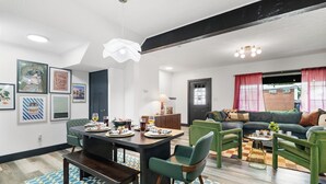 A modern living room with a sofa, chairs, a dining table set with plates and glasses, and artwork on the walls. - The Play Haus! Hot Tub, Game Room, Firepit, Families (Columbus)