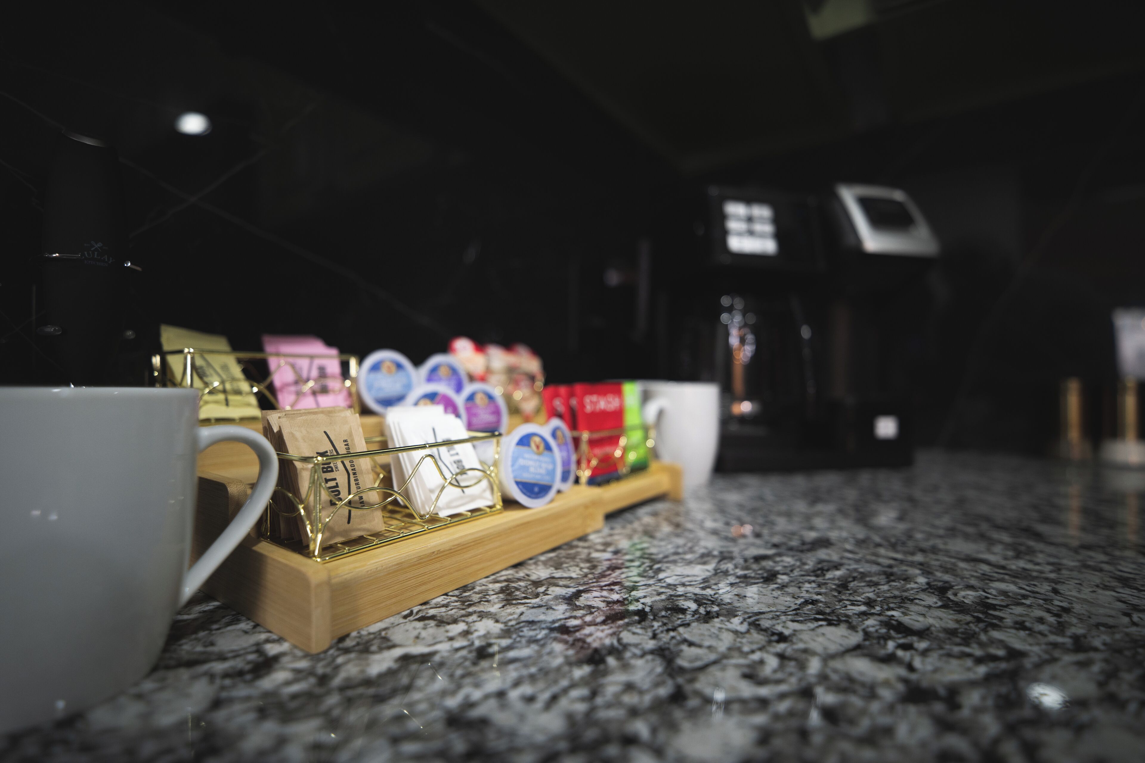 A coffee station with a tray of coffee pods and a white mug on a granite countertop.