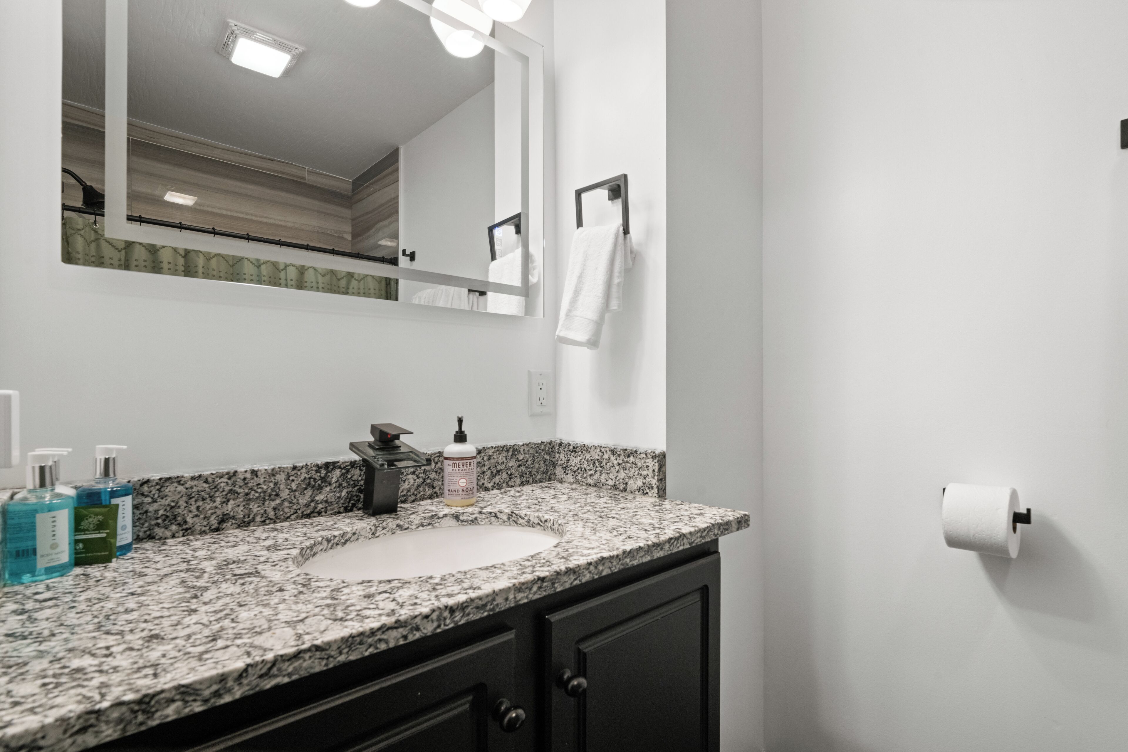 A bathroom with a granite countertop, a sink, a mirror, a towel rack, and toiletries.