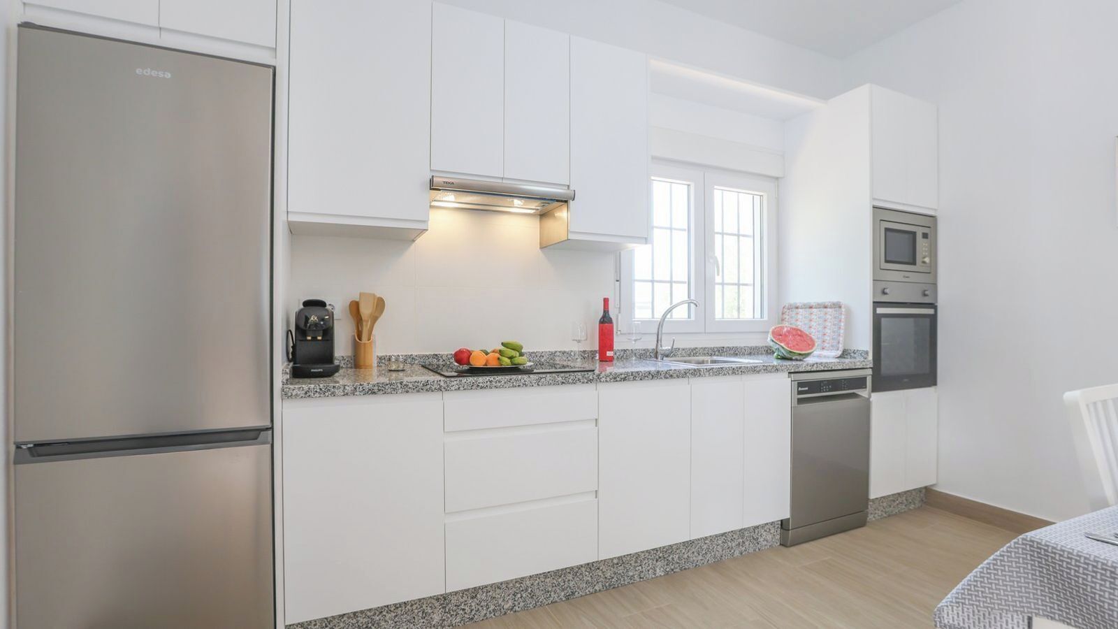 A modern kitchen with white cabinets, a stainless steel refrigerator, a built-in microwave, and a dishwasher.