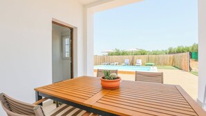 Een houten tafel met stoelen en een potplant in een kamer met uitzicht op een zwembad en terras.