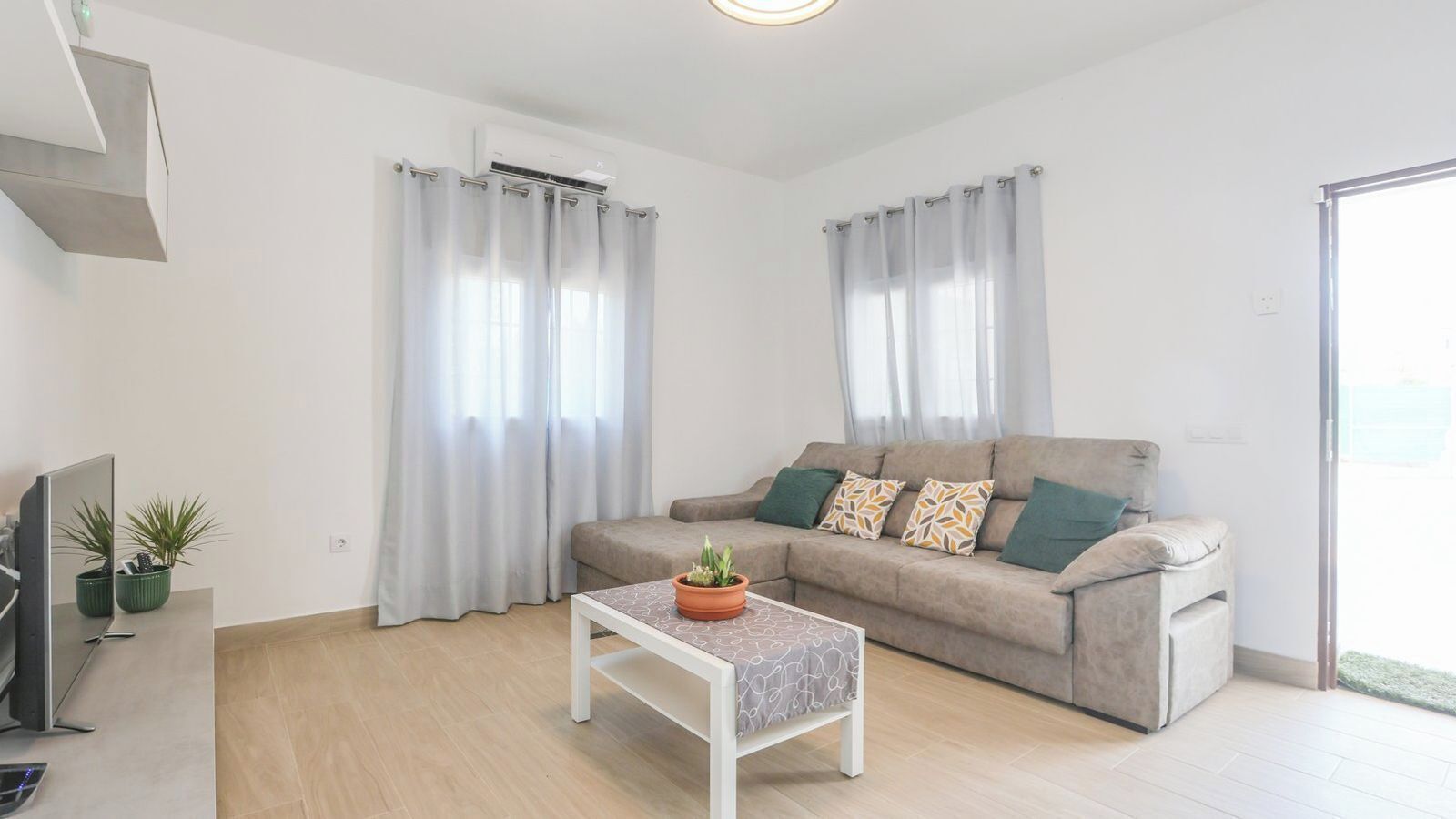 A modern living room with a sofa, a coffee table with a plant, and a TV on a stand.